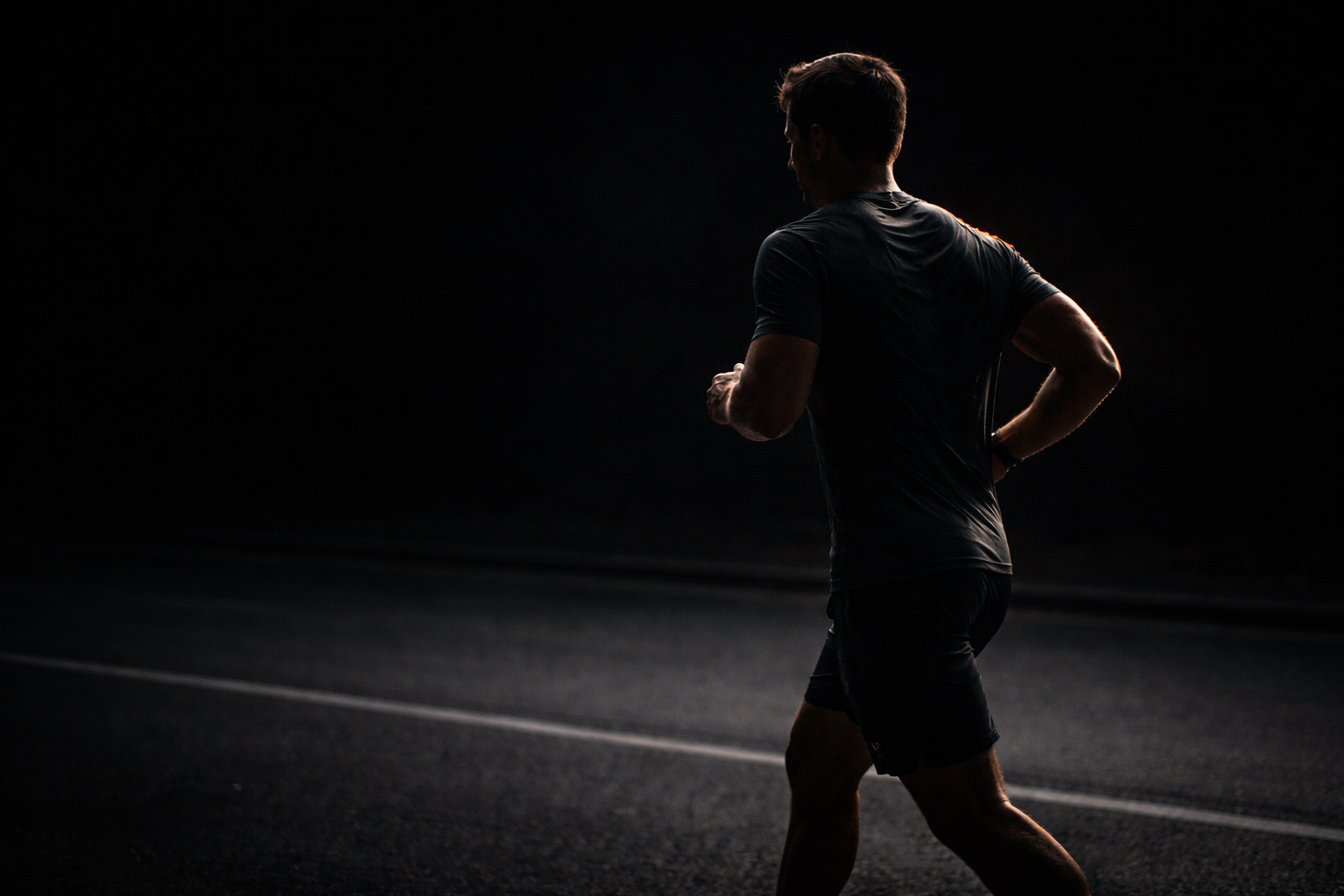 Male runner at steady pace in dark environment — sustained Zone 2 training for mitochondrial biogenesis
