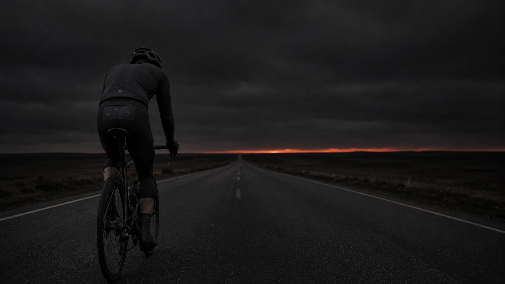 Lone cyclist slowing on a dark empty road with orange light on the horizon — hitting the wall from glycogen depletion