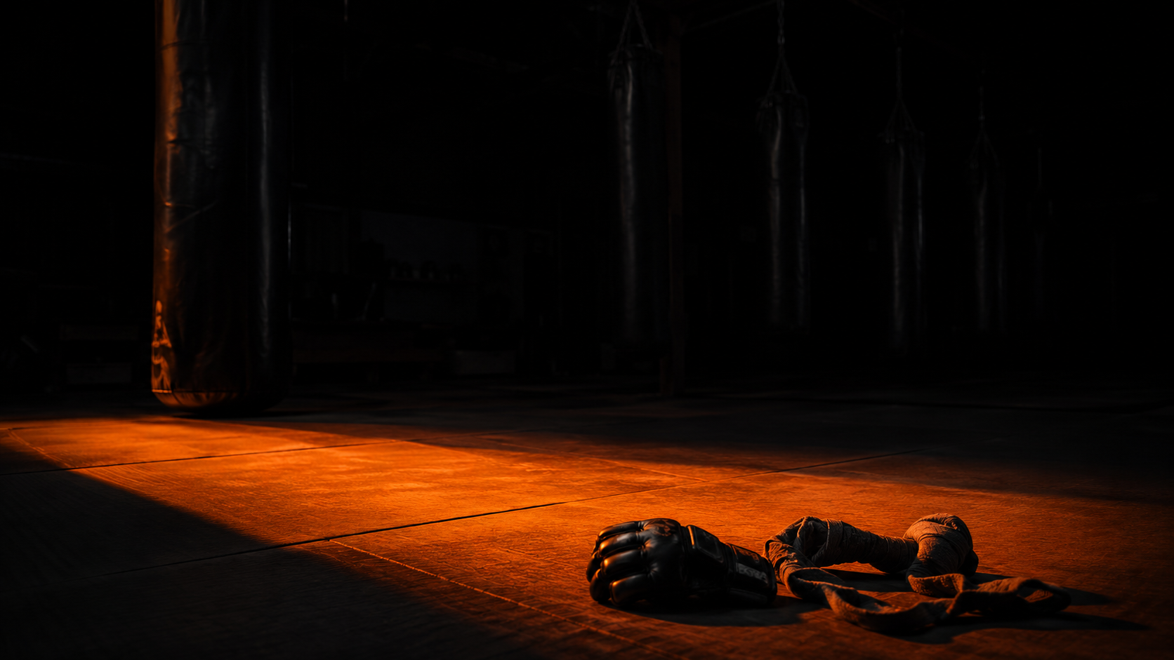 Empty dark training space with abandoned boxing equipment, orange-lit training mat in foreground