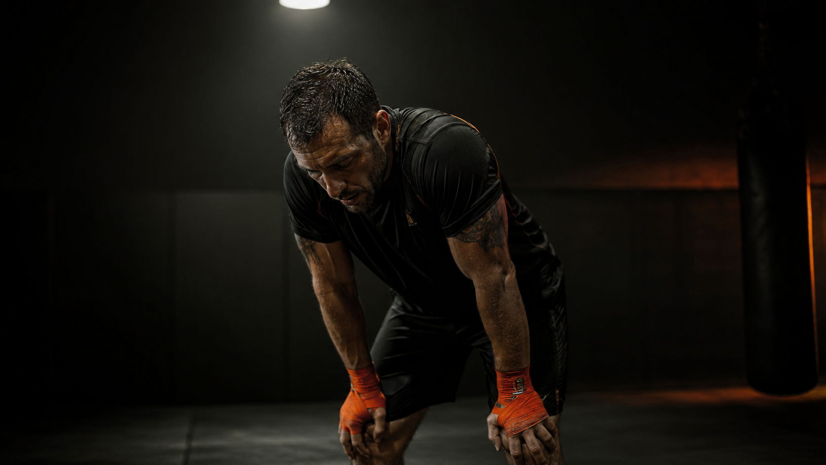 Fatigued combat sports athlete mid-session, depleted posture, sparse dark gym environment